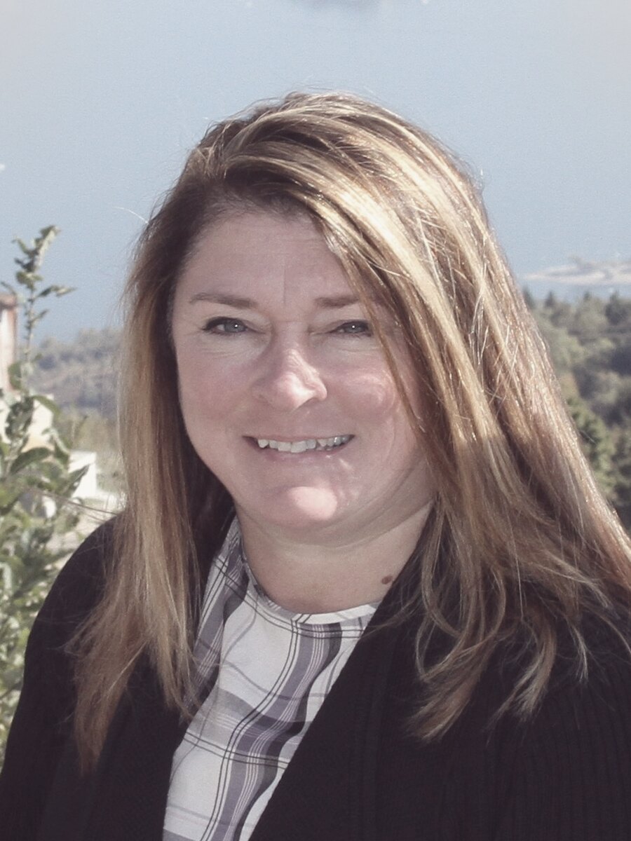 Patty Anderson, photographed outdoors in three-quarter view against water and a hillside, wearing a dark jacket over a checked shirt. The image is printed in a single warm tone rather than full color.