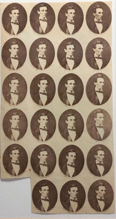 An uncut sheet of twenty-three small oval photographs of Abraham Lincoln, beardless, all printed from the same negative in warm brown on cream paper. They sit in five rows of four with three more below. A line of tiny printed text runs under each oval. The lower left corner of the sheet has been cut away where prints were removed.